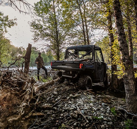 A person pulling out a tree stump using a chain connected to the rear hitch of their 2027 Polaris RANGER 1000 Premium UTV.
