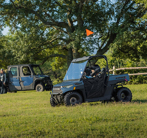 2 kids in a 2027 Polaris RANGER 150 EFI youth UTV while their parents watch in the background.