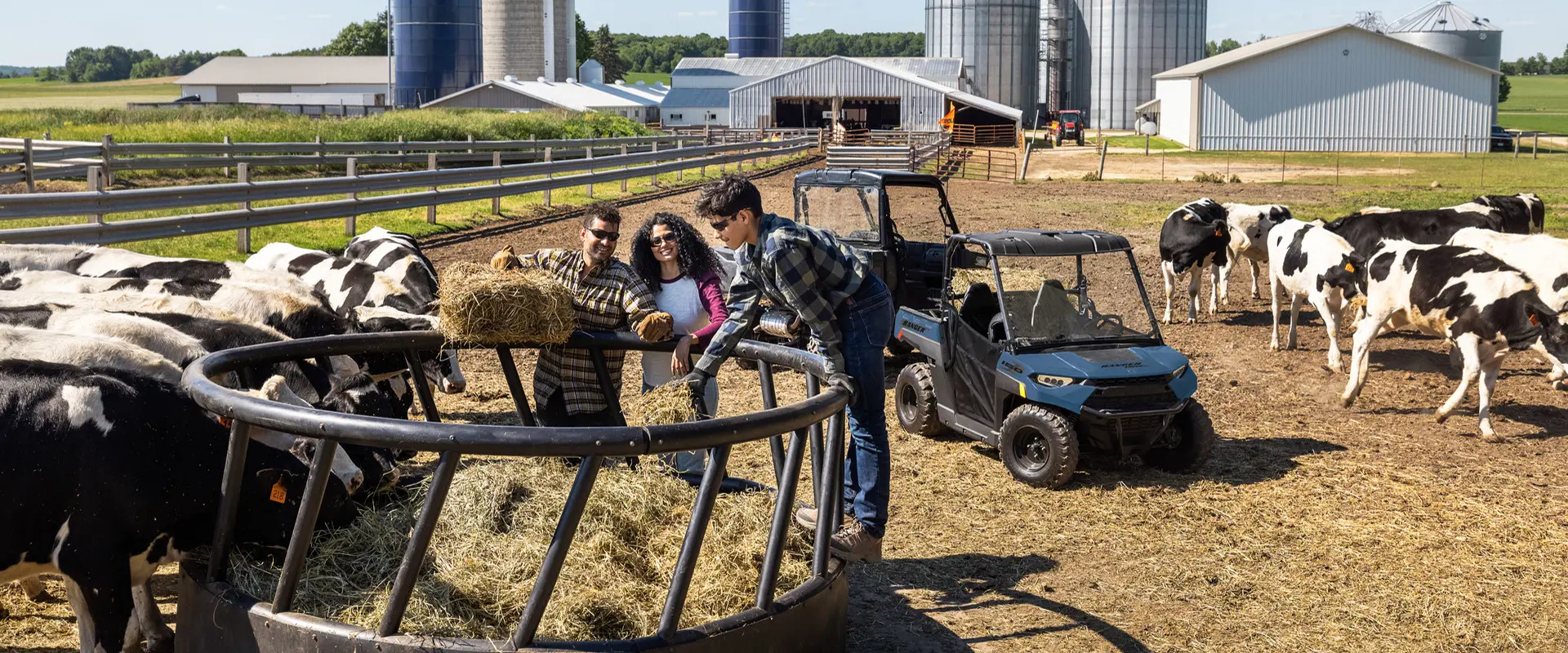 A kid standing on a bale ring with his 2027 Polaris RANGER 150 EFI youth UTV in the background near cows.