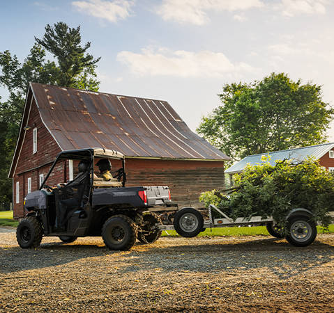 2 riders in a 2027 Polaris RANGER 500 UTV pulling a trailer with tree debris on a farm.