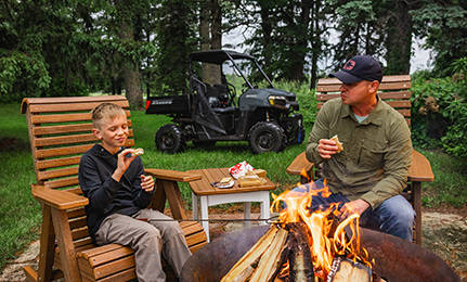A man and his son having smores by a fire while their 2027 Polaris RANGER 500 UTV is parked behind them.
