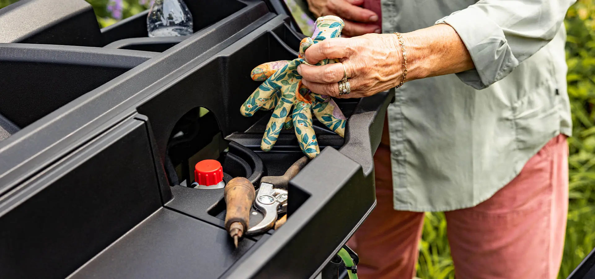 A woman grabbing gardening gloves from a storage area in her 2027 Polaris RANGER 500 UTV.