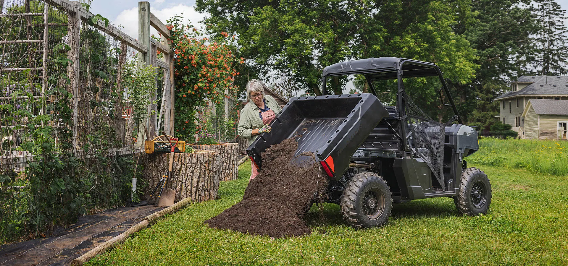 A woman dumping black dirt out of the cargo box of a 2027 Polaris RANGER 500 UTV.