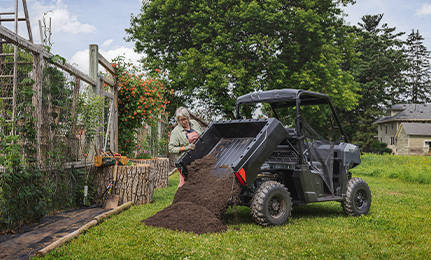 A woman dumping black dirt out of the cargo box of a 2027 Polaris RANGER 500 UTV.