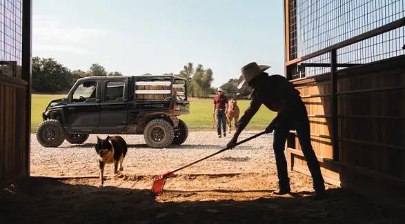 Un agricultor limpiando un granero con un UTV Polaris RANGER CREW XD 1500 NorthStar Texas Edition 2027 para uso extremo al fondo.