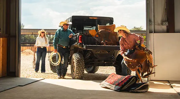 Tres personas cargando equipo para montar a caballo en la caja de carga de un UTV Polaris RANGER CREW XD 1500 NorthStar Texas Edition 2027 de uso extremo.