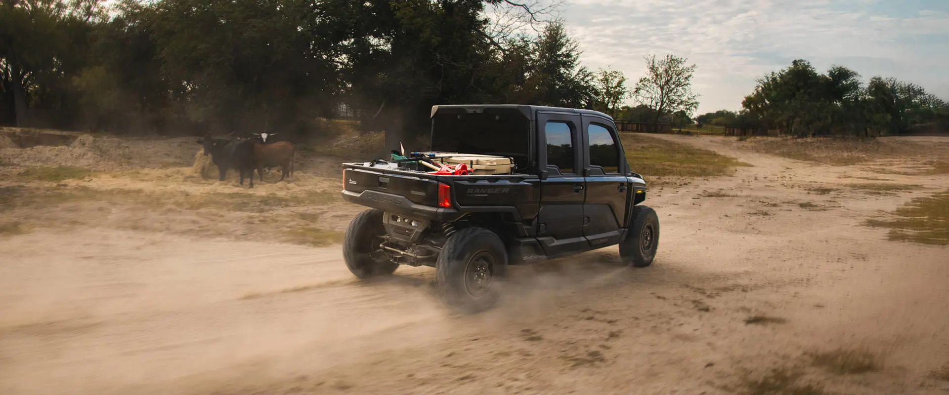 Un UTV Polaris RANGER CREW XD 1500 NorthStar Texas Edition 2027 para uso extremo circulando por un camino de tierra en una granja.