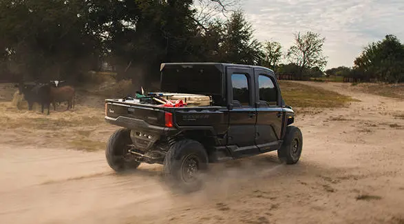 Un UTV Polaris RANGER CREW XD 1500 NorthStar Texas Edition 2027 para uso extremo circulando por un camino de tierra en una granja.