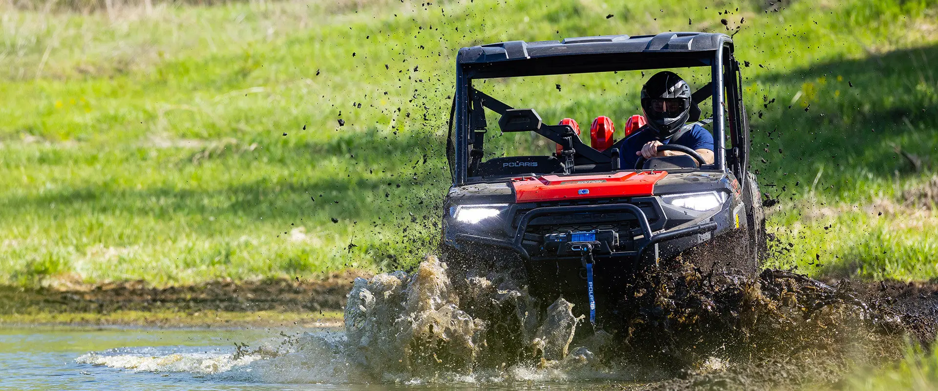 A rider in a 2027 Polaris RANGER CREW XP 1000 Mud Edition UTV driving through a deep mud puddle.