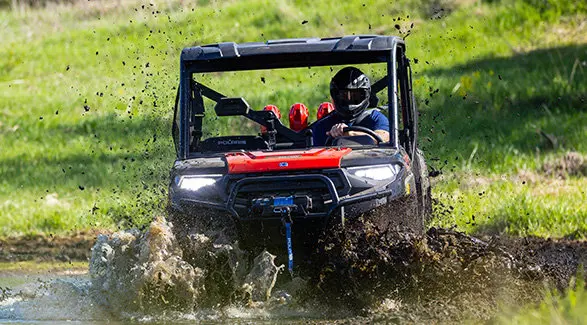 A rider in a 2027 Polaris RANGER CREW XP 1000 Mud Edition UTV driving through a deep mud puddle.
