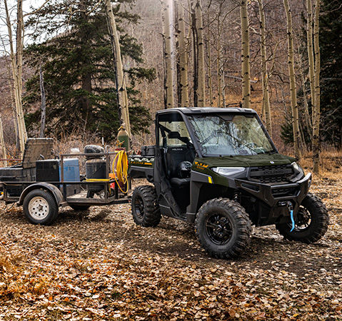 A woman loading gear onto a trailer being pulled by a 2027 Polaris RANGER XP 1000 UTV.