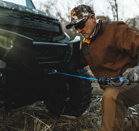 A man using the winch from the front-end of a 2027 Polaris RANGER XP 1000 UTV.