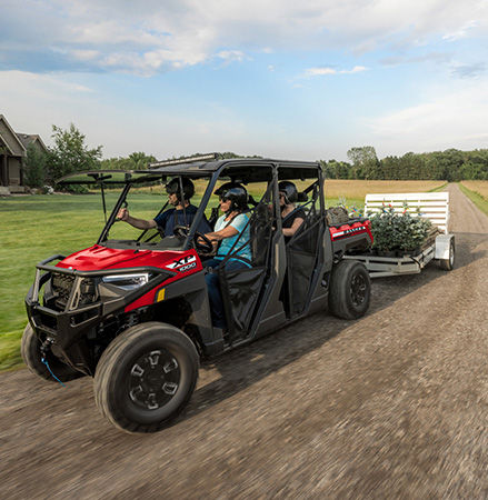4 people in a 2027 Polaris RANGER XP 1000 UTV pulling a trailer loaded with tree debris.