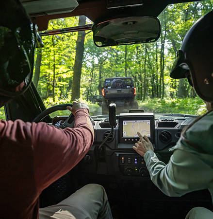 A person using the RIDE COMMAND touch screen in the cab of a 2027 Polaris RANGER XP 1000 NorthStar Trail Boss Edition UTV.