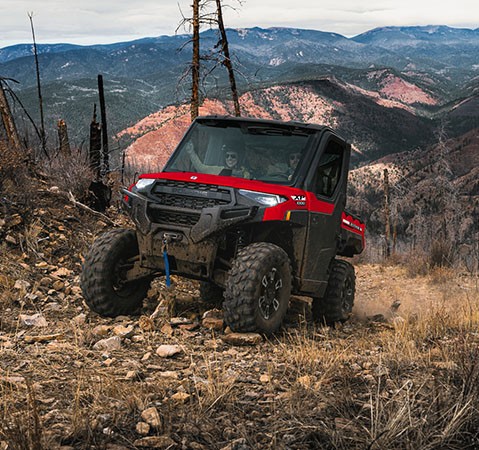 A 2027 Polaris RANGER XP 1000 NorthStar enclosed UTV climbing over rocky terrain with 29-inch Pro Armor X Terrain tires.