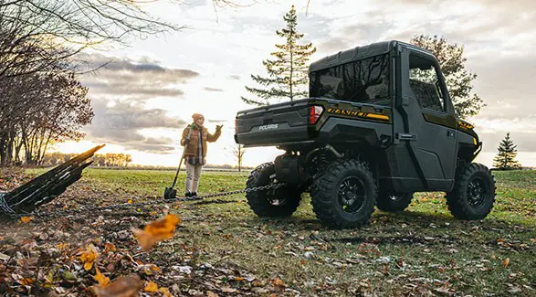 A 2027 Polaris RANGER XP 1000 NorthStar enclosed UTV pulling out a stump with a chain attached to the rear hitch.