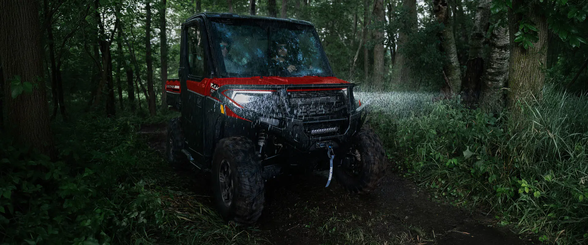 2 riders in a 2027 Polaris RANGER XP 1000 NorthStar enclosed UTV driving through a forest in the rain at night.