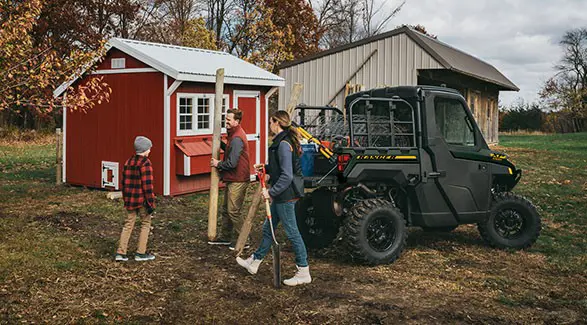 A family using their 2027 Polaris RANGER XP 1000 NorthStar enclosed UTV to haul fence posts and fence.
