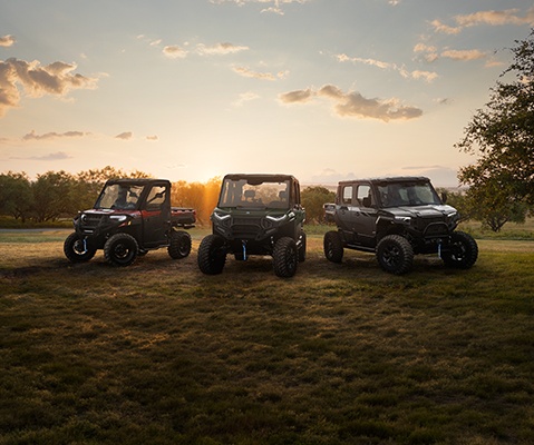 A lineup of three Polaris RANGER UTVs are displayed on a grassy field at sunset, showcasing Polaris utility and adventure off-road vehicles.