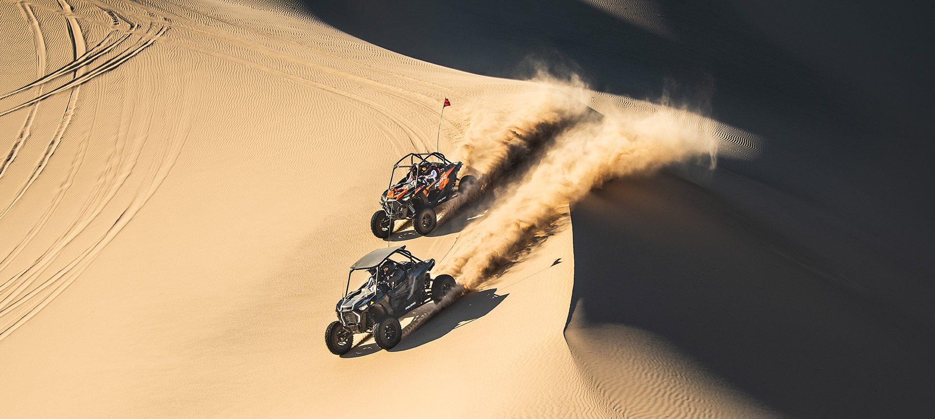 Two RZR vehicles side by side in the sand