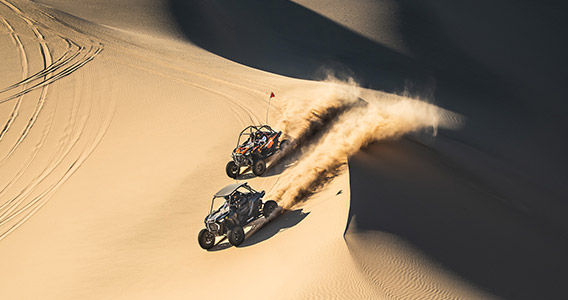 Two RZR vehicles side by side in the sand