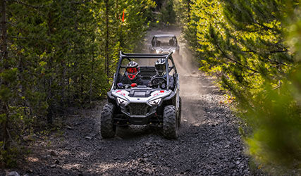 2 RZR 200's riding down a trail with bright LED headlights