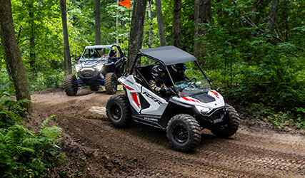 2 kids in a Polaris RZR 200 leading on a forest trail
