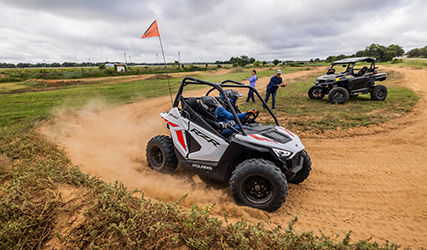2 kids driving on a dirt track in their Polaris RZR 200