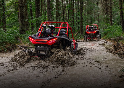RZR XP 1000 High Lifter performing in a mud-laden terrain through a forest.