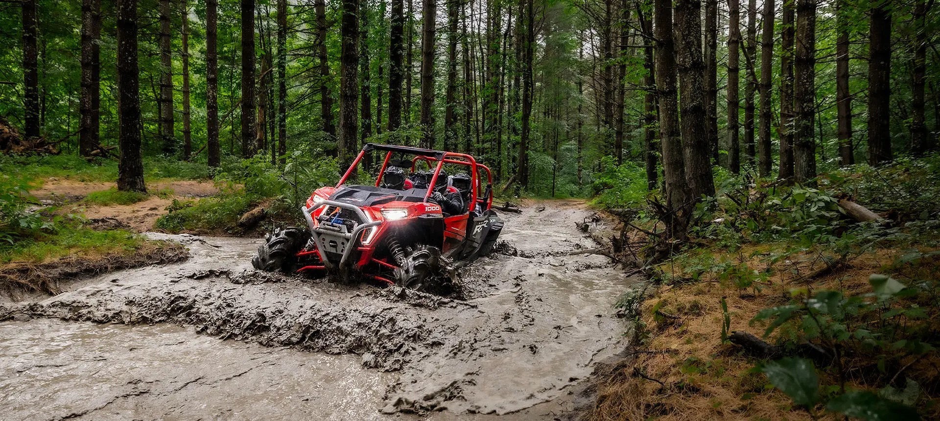 RZR XP 1000 High Lifter going through a muddy lake between a route.