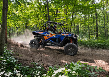 blue and orange rzr xp 1000 driving on a forest trail