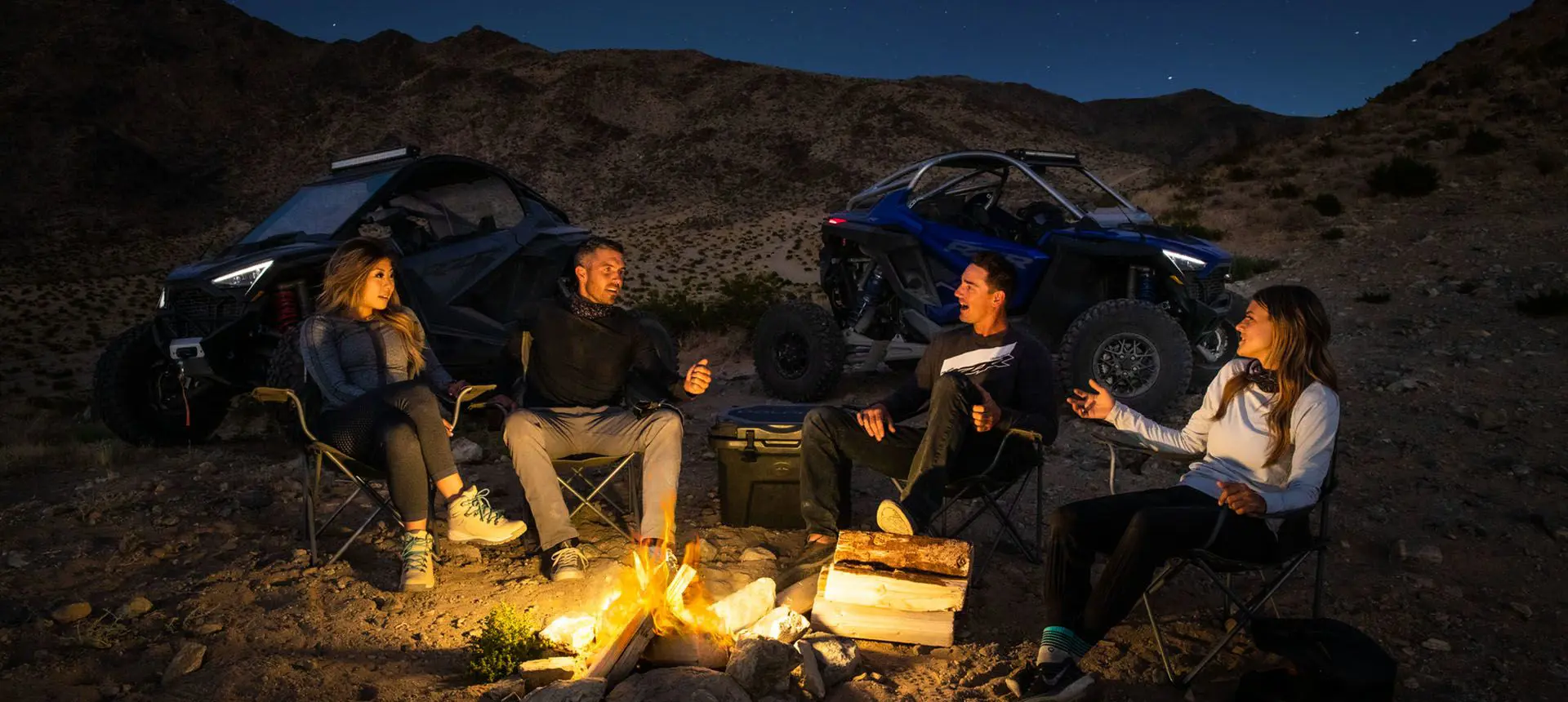 amigos alrededor del fuego con su polaris rzr pro r side by sides en la cercanía