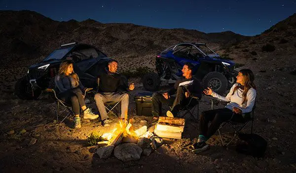 amigos alrededor del fuego con su polaris rzr pro r side by sides en la cercanía