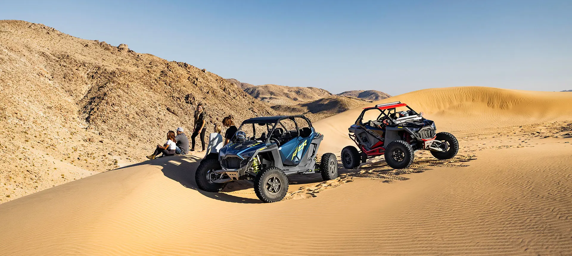 riders taking a break near their polaris rzr turbo r 4 side by sides in the dunes