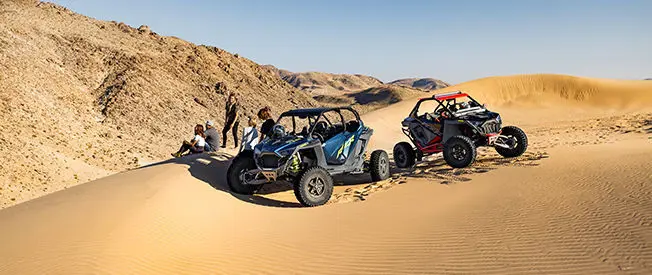 riders taking a break near their polaris rzr turbo r 4 side by sides in the dunes