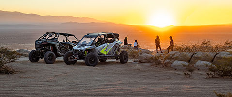 A group of friends standing near their RZR Turbo R and RZR Turbo R 4, enjoying the desert sunset