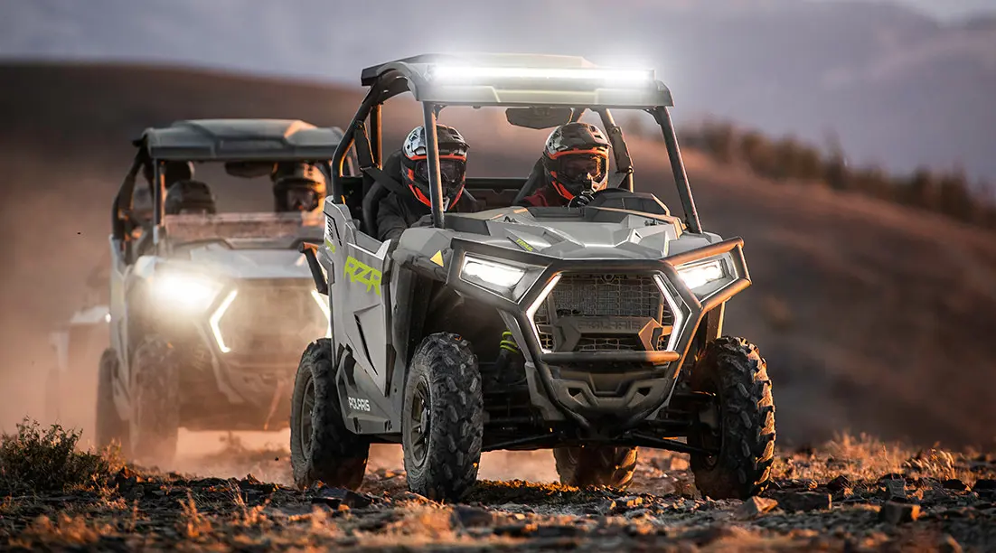 riders in a rzr trail side by side with headlights and light bar illuminated