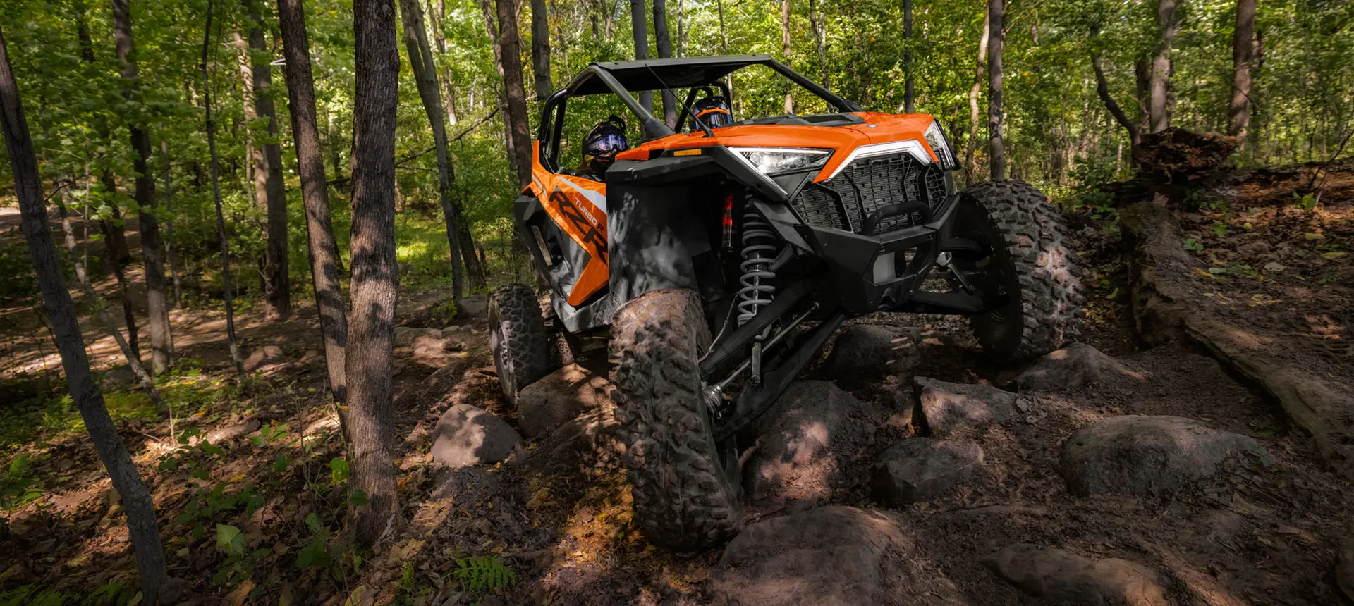 vue de face d’un côte à côte RZR Pro R orange sur un terrain forestier rocheux