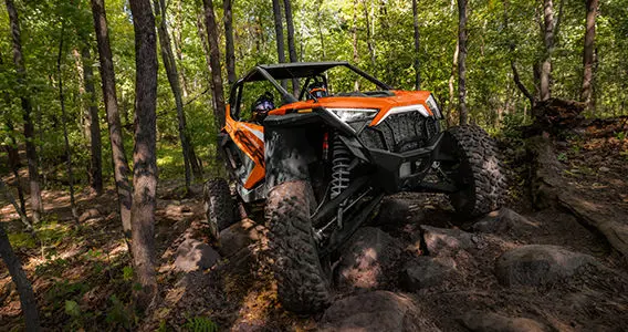 vue de face d’un côte à côte RZR Pro R orange sur un terrain forestier rocheux