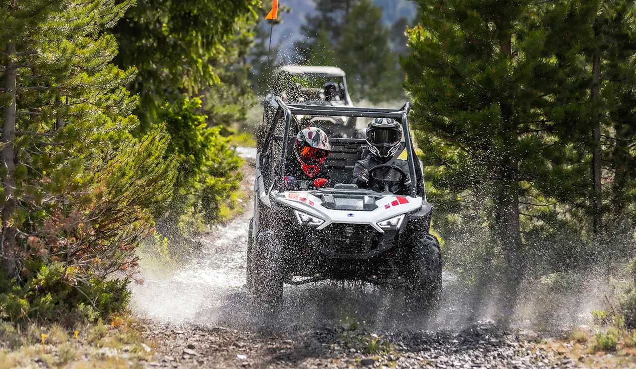 enfants traversant une flaque de boue dans un côte à côte RZR 200