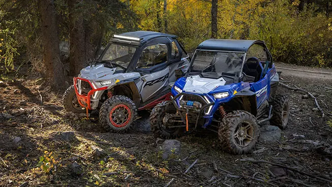 RZR Trail and Trail S side by sides parked near a trail