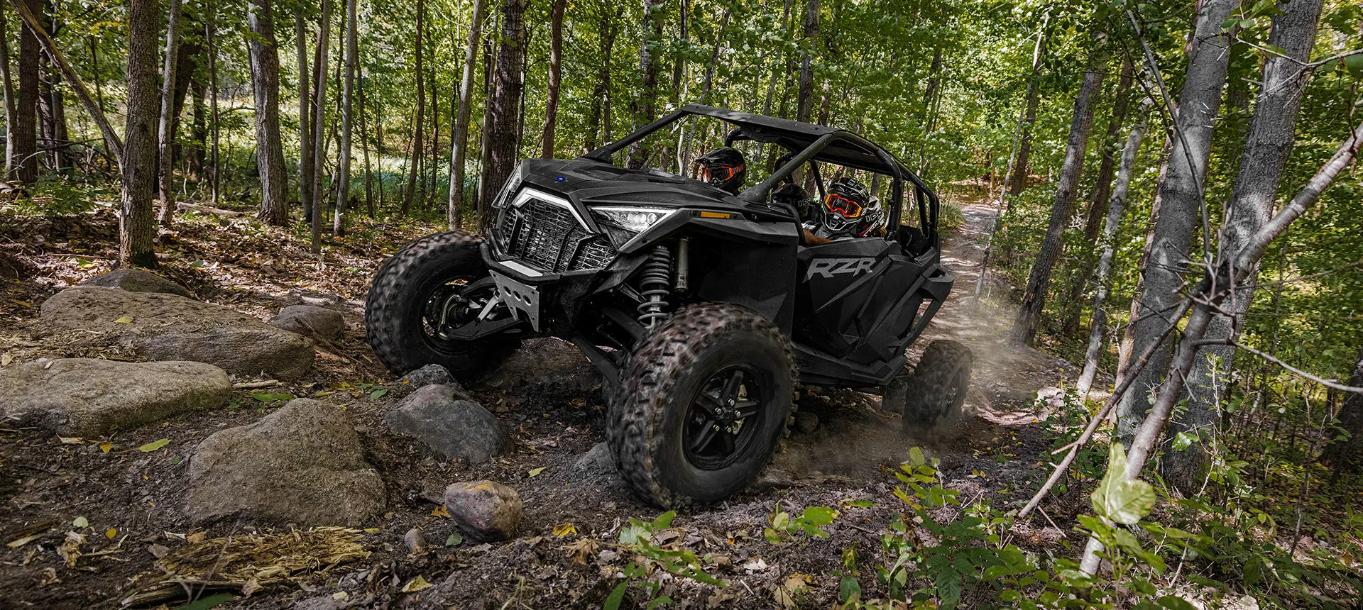 un side by side rzr turbo r 4 en negro ónix conduciendo por un sendero rocoso del bosque
