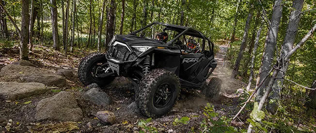un side by side rzr turbo r 4 en negro ónix conduciendo por un sendero rocoso del bosque