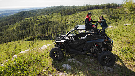 A man helping a woman get on a RZR Pro R in the greenfield