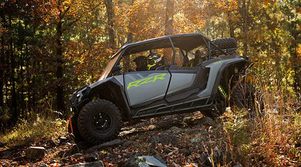 Side profile of a storm gray 2025 RZR XP 4 side by side in a forest.