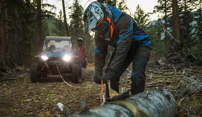 man using his polaris rzr trail s side by side winch to move a log