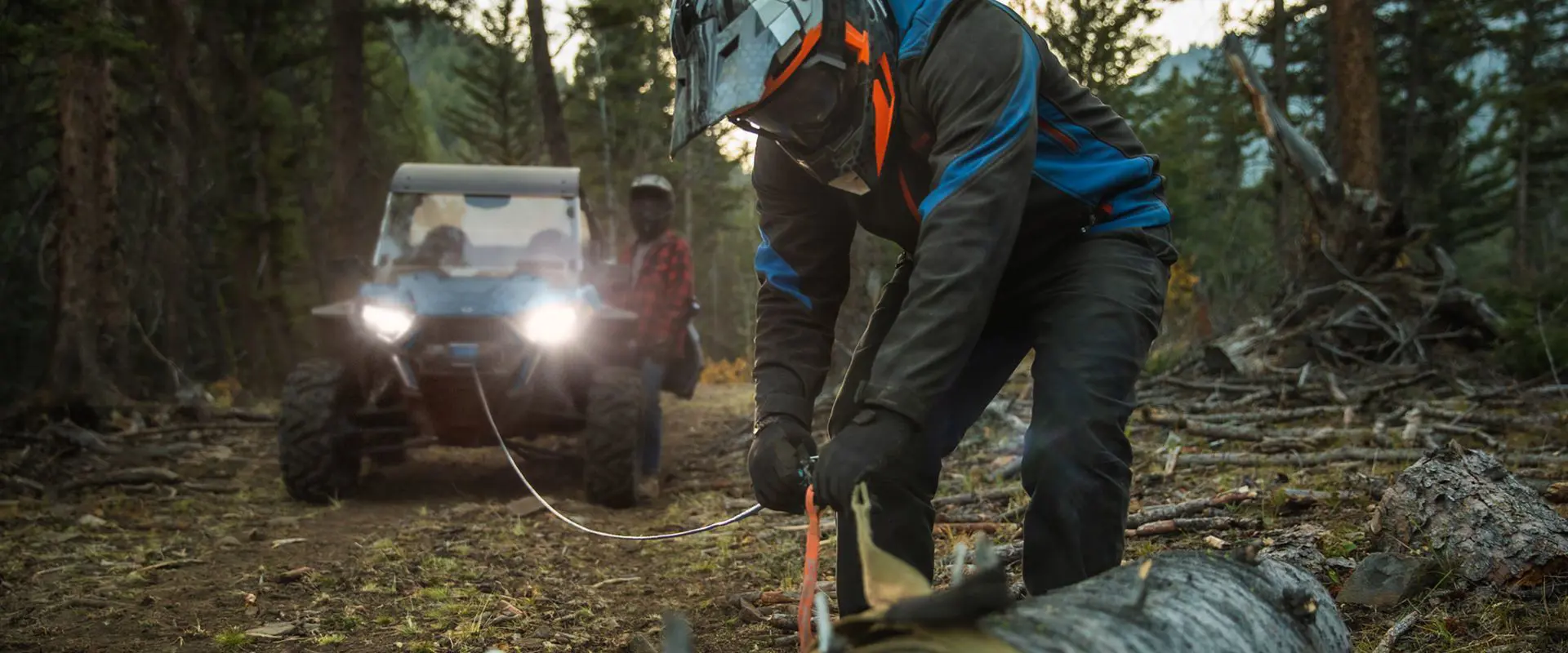 man using his polaris rzr trail s side by side winch to move a log