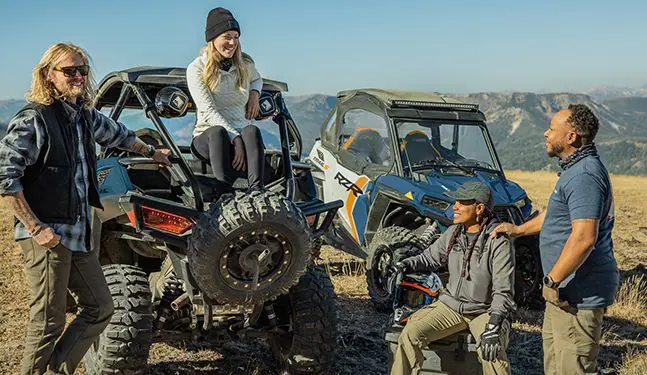 people relaxing aroudn their polaris rzr trail s side by sides