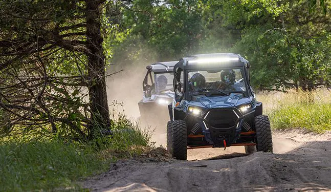 2 polaris trail s side by sides driving on a trail