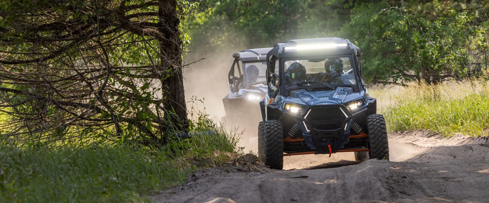 2 polaris trail s side by sides driving on a trail